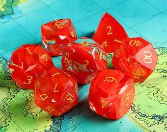 Puede incluir: Conjunto de siete dados poliédricos rojos y dorados para juegos de mesa. Los dados tienen numeración dorada y un efecto veteado. Están colocados sobre una superficie con mapa.