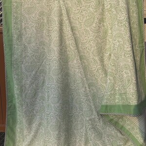 May include: A light green and white paisley patterned textile. The textile has a border of solid light green with a black and white rope trim. The paisley pattern is a repeating design of curved, teardrop-shaped motifs.