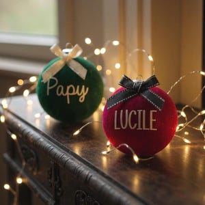 May include: Two round velvet Christmas ornaments, one dark green with the white text Papy and a cream ribbon, and one deep red with the white text LUCILE and a black ribbon, both featuring a metallic top loop for hanging.