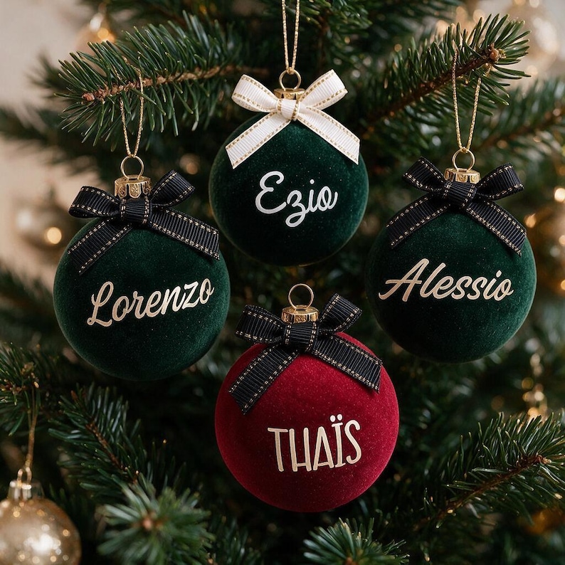 May include: Four spherical Christmas ornaments with a velvet texture. Three are dark green with black bows and gold lettering reading Lorenzo, Ezio, and Alessio. One is deep red with a black bow and gold lettering reading THA&Iuml;S.