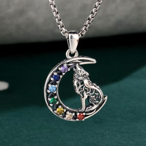 May include: A silver-colored pendant necklace featuring a howling wolf silhouette on a crescent moon. The moon is adorned with a rainbow of colorful gemstones. The necklace has a delicate chain and the brand name "Labellry Handmade Jewelry" is visible.