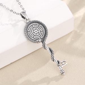 May include: A silver pendant necklace with a key design. The key has a circular top with a maze pattern and a twisted stem. The necklace is displayed on a white surface. The brand name "Labellry Handmade Jewelry" is visible in the top right corner.