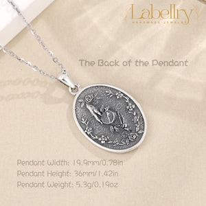 May include: Silver pendant necklace with an oval pendant featuring a hand holding a pomegranate, surrounded by floral details. The pendant is 0.78 inches wide and 1.42 inches high. The text "The Back of the Pendant" is visible.