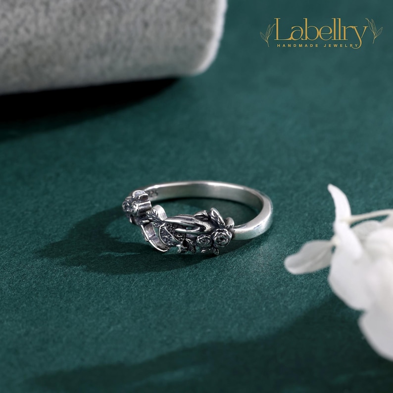 May include: A silver ring featuring an intricate, oxidized floral design with sculpted rose motifs along the band. The metal has a darkened finish in the recessed areas to highlight the detailed petal textures. The text Labellry Handmade Jewelry is visible.