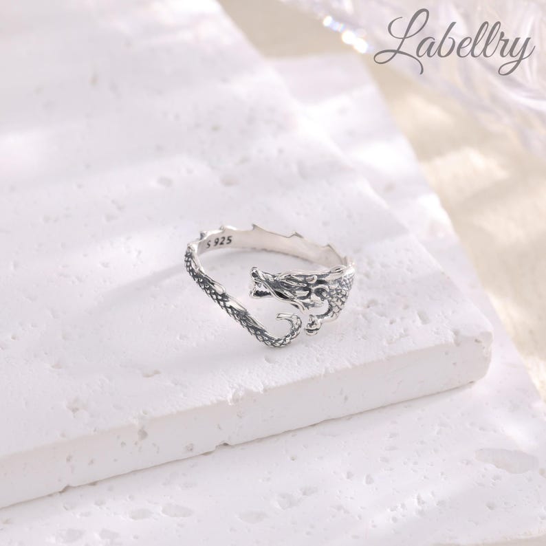 May include: Silver dragon ring with a detailed design. The ring is open on one side and has the inscription "S 925" on the inside.