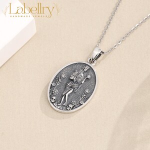 May include: A silver-toned pendant necklace featuring an oval pendant with a detailed relief of a woman holding flowers, surrounded by floral and skull motifs. The necklace has a delicate chain and the brand name "Labellry" is visible in the upper left corner.
