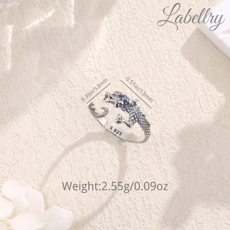 May include: Silver dragon ring with a textured finish. The ring is adjustable and measures 0.39 inches in diameter. The ring is marked with "S 925" and weighs 2.55 grams.