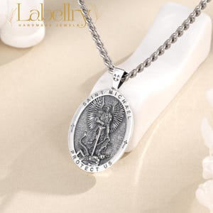 Pu&ograve; includere: Collana con pendente argentato con un medaglione ovale di San Michele. Il medaglione raffigura San Michele che uccide un drago, con le parole "SAINT MICHAEL PROTECT US". La collana ha una catena strutturata e una chiusura.