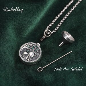 May include: A silver-colored pendant necklace with a round locket featuring an elephant design with green accents. The necklace includes a chain, a small funnel, and a tool. The text "Tools Are Included" is visible.