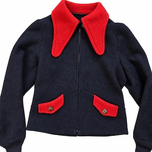 May include: A dark navy blue jacket featuring a large, pointed red collar, a central zip fastening, and two front pockets with red flaps secured by brown buttons. The sleeves have ribbed cuffs, and the overall construction is a solid, textured fabric.