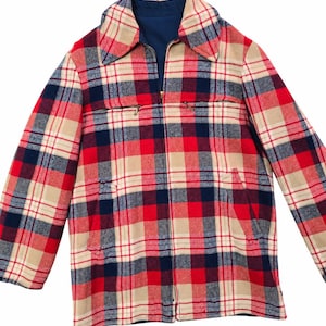 May include: A long-sleeve jacket featuring a plaid pattern in red, navy blue, and beige. The jacket has a pointed collar, a full-length front zip, two horizontal zipped chest pockets, and two vertical side pockets with a solid navy blue lining.