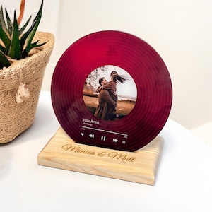 May include: A red vinyl record with a photo of a couple in a field. The record has a music player interface with the text "Your Artist" and "Your Song". The record is on a wooden stand with the text "Monica & Matt" engraved on it.