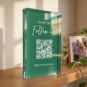 Op de afbeelding: Een rechthoekig, helder acrylblok met een diepgroene achtergrond. De tekst luidt SCAN TO Follow us in het wit, met een centrale witte QR-code en de gebruikersnaam @yourbusiness in het wit onderaan het display gedrukt.