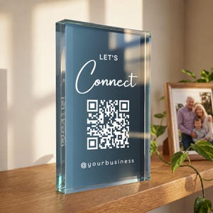 May include: A rectangular clear acrylic block sign featuring a deep blue background with white text that reads LET'S Connect, a central white QR code, and the text @yourbusiness at the bottom. The sign has a smooth, polished finish.
