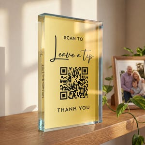 May include: A rectangular clear acrylic block sign with a yellow insert featuring black text that reads SCAN TO Leave a tip and THANK YOU, centered above and below a black and white QR code. The sign has a thick, transparent border.