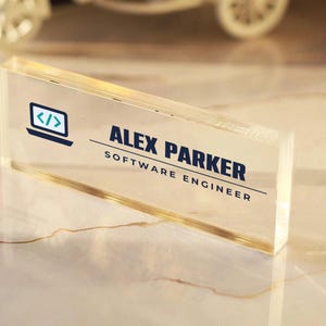May include: A rectangular clear acrylic desk name plate featuring a dark blue graphic of a laptop with code brackets, the name ALEX PARKER, and the job title SOFTWARE ENGINEER printed in dark blue text with horizontal lines.