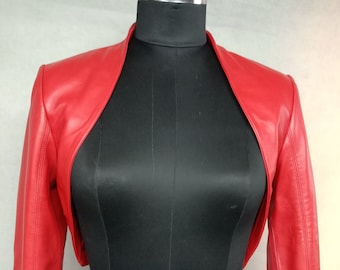 May include: A red leather bolero with long sleeves. The bolero is cropped at the waist and has a shawl collar.