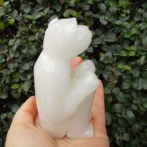 May include: A white, carved alabaster sculpture of a monkey sitting with its arms crossed. The sculpture is smooth and polished.