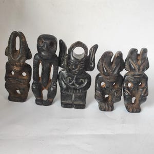 May include: Five dark-colored, carved figurines with unique shapes and designs. The figurines appear to be made of stone or a similar material, with varying levels of detail and wear. Each figure has a distinct form, suggesting a collection of artistic or cultural artifacts.