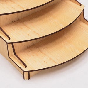 May include: A wooden tiered stand with four shelves. The shelves are curved and have a dark brown trim. The stand is made of light wood with a natural finish.