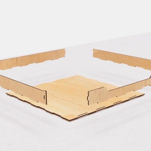 May include: A wooden box with four sides and a base. The sides are assembled to form a square shape. The box is made of light brown wood with a natural finish.