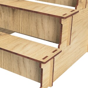 May include: Wooden three-tiered shelf unit with a natural wood finish. The shelf unit is made of plywood and has a simple, modern design.