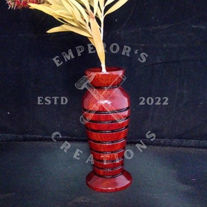 May include: A red wooden vase with a striped design. The vase is filled with dried flowers. The vase is labelled "Emperor's Creations Est. 2022".