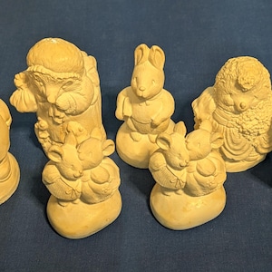 Peut inclure: Ensemble de sept figurines en céramique, chacune représentant un animal différent. Les figurines sont peintes dans une couleur beige clair et ont un aspect rustique et vintage. Les animaux comprennent un hibou, un hérisson, un lapin, une grenouille et trois souris.