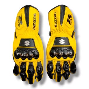 May include: A pair of yellow leather motorcycle gloves with black accents and the word "SUZUKI" printed on the back of each glove.