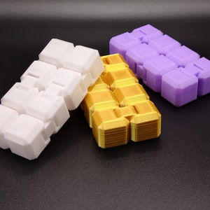 May include: Three interlocking puzzle cubes in white, gold, and purple. The cubes are made of plastic and have a smooth, matte finish.
