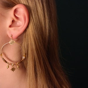 May include: Gold hoop earrings with brown and white beads and a star charm.