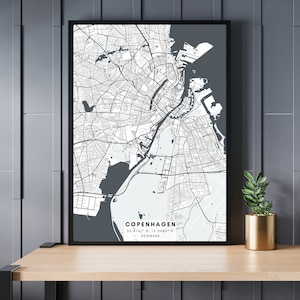 May include: A black and white map of Copenhagen, Denmark, with the city's name and coordinates printed at the bottom. The map is framed in a black frame and is hanging on a grey wall.