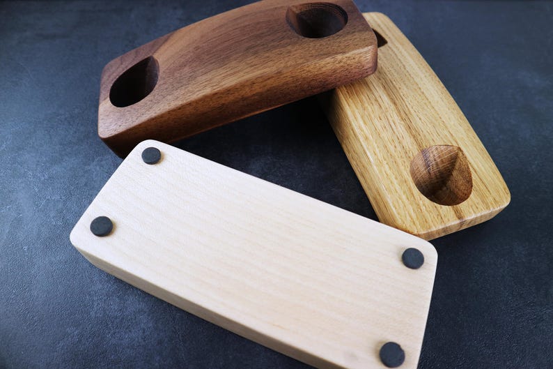 May include: Three wooden coasters with rounded edges and a single hole in the center. The coasters are made of different types of wood: walnut, oak, and maple. Each coaster has four black rubber feet on the bottom.