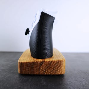 May include: A black and white video game controller sits on a wooden stand. The stand is made of light brown wood with a natural grain.