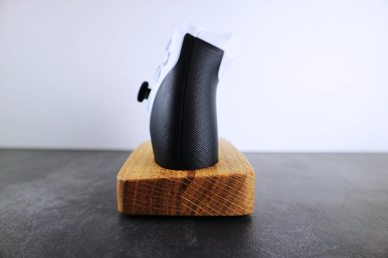 May include: A black and white video game controller sits on a wooden stand. The stand is made of light brown wood with a natural grain.