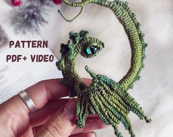 May include: Green crocheted dragon amigurumi with a curled tail and wings. The dragon has a green eye with a blue pupil. The pattern is available as a PDF and video.