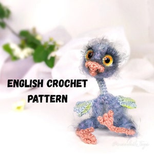 May include: Crocheted amigurumi ostrich toy with blue and green feathers, pink feet, and large orange eyes. The toy is sitting on a white surface with the text "ENGLISH CROCHET PATTERN" in black.