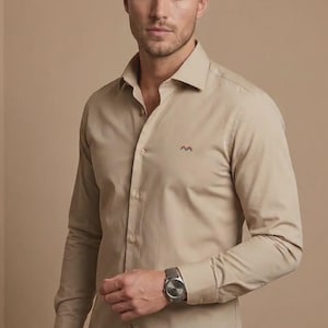 Op de afbeelding: Een beige overhemd met lange mouwen, knoopsluiting, een klassieke kraag en een klein geborduurd logo op de linkerborst. Het overhemd wordt gecombineerd met een blauwe spijkerbroek en een zilverkleurig polshorloge met een donkere wijzerplaat.