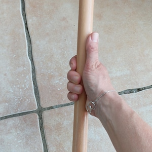 Op de afbeelding: Een houten deegroller, ongeveer 38 cm lang, wordt in een hand gehouden. De deegroller is lichtbruin van kleur en heeft een glad oppervlak.