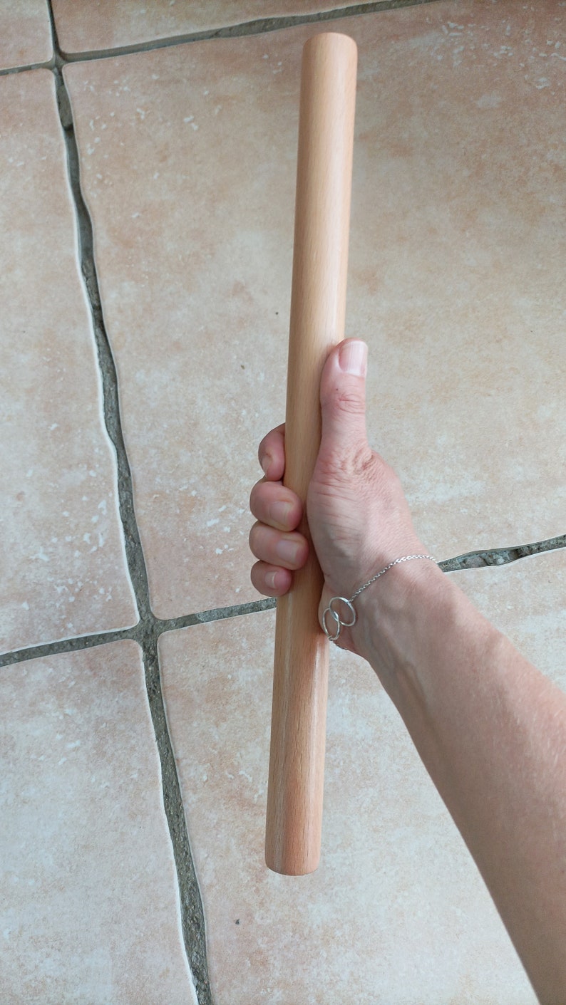 Op de afbeelding: Een houten deegroller, ongeveer 38 cm lang, wordt in een hand gehouden. De deegroller is lichtbruin van kleur en heeft een glad oppervlak.