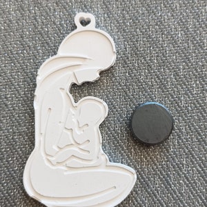 May include: White ceramic ornament depicting a mother holding a child. The ornament is in the shape of a silhouette and has a heart-shaped hole at the top.