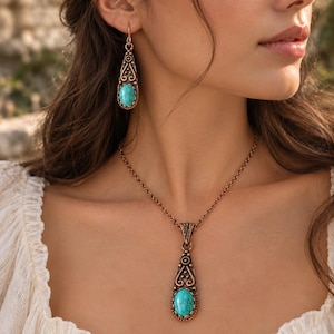 May include: A copper-toned jewelry set consisting of a pendant necklace and a matching drop earring. Each piece features an elongated, teardrop-shaped metal frame with intricate scrollwork and a central, oval-cut turquoise stone with dark veining.