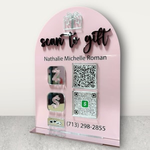 May include: A pink acrylic sign with the text "scan to gift" in black script. The sign includes a gift box graphic, the name "Nathalie Michelle Roman", QR codes, and payment app logos. The phone number (713) 298-2855 is also displayed.