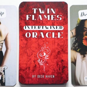 May include: Three oracle cards from the Twin Flames Intertwined Oracle deck. The first card shows a woman tied up with rope and the text "All Tied Up" and "I Feel Stuck". The second card has a red background with a white snake and crescent moon design and the text "Twin Flames Intertwined Oracle" and "By Deck Haven". The third card shows a woman with flowers in her hair and the text "Divine Feminine" and "Tuned In Woman".