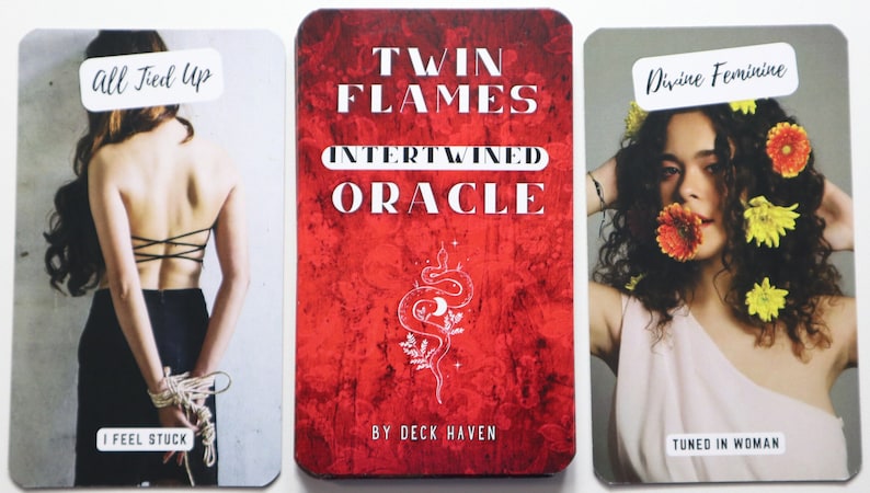 May include: Three oracle cards from the Twin Flames Intertwined Oracle deck. The first card shows a woman tied up with rope and the text "All Tied Up" and "I Feel Stuck". The second card has a red background with a white snake and crescent moon design and the text "Twin Flames Intertwined Oracle" and "By Deck Haven". The third card shows a woman with flowers in her hair and the text "Divine Feminine" and "Tuned In Woman".