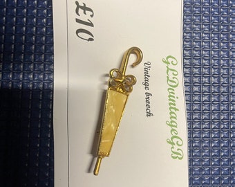 May include: A gold-toned vintage brooch shaped like an umbrella with a white and yellow design. The brooch is on a white card with the text "Vintage brooch" and "£10".