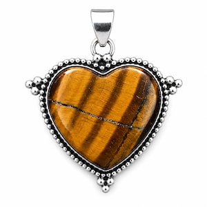 May include: A heart-shaped tiger's eye gemstone pendant set in a polished silver frame. The stone features brown and golden-yellow bands with a smooth, polished surface. The silver border is decorated with small, raised metal beads and a bail.