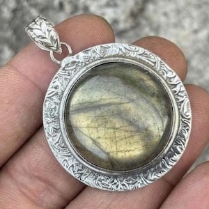 May include: A round pendant featuring a polished, iridescent labradorite gemstone set within a silver-toned metal frame. The frame displays an intricate, embossed leaf-like pattern and includes a decorative, textured bail at the top.
