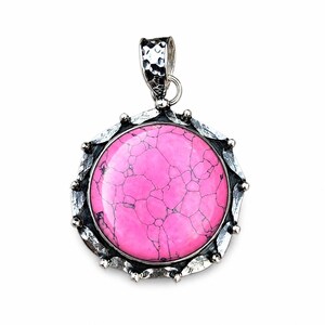 May include: A round pendant featuring a vibrant pink stone with dark veining, set in a textured, oxidized silver frame. The metal border has a scalloped edge with small silver beads, and the top includes a hammered silver bail for hanging.