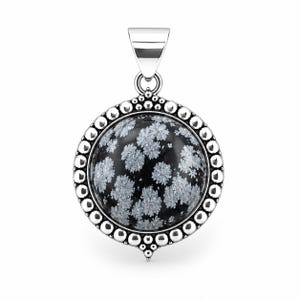 May include: A round pendant featuring a polished black snowflake obsidian stone with white, star-like inclusions. The stone is set in a silver frame decorated with a beaded border and a smooth, tapered silver bail at the top for hanging.